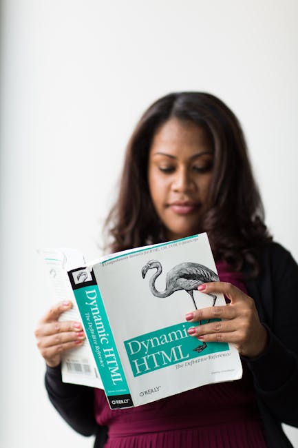 A woman with long dark hair and medium skin tone is holding a book titled 'Dynamic HTML' by O'Reilly, which features a detailed illustration of a flamingo on the cover. She is dressed in a dark blazer